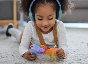 Learning, playing and child with headphones or toys for development, sensory stimulation or helping. Girl kid, psychology therapy and emotion regulation with fun music in clinic for adhd diagnosis.